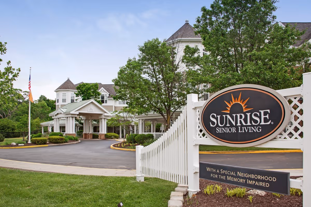 Exterior view of the Sunrise Senior Living building and entrance with a large sign and driveway.