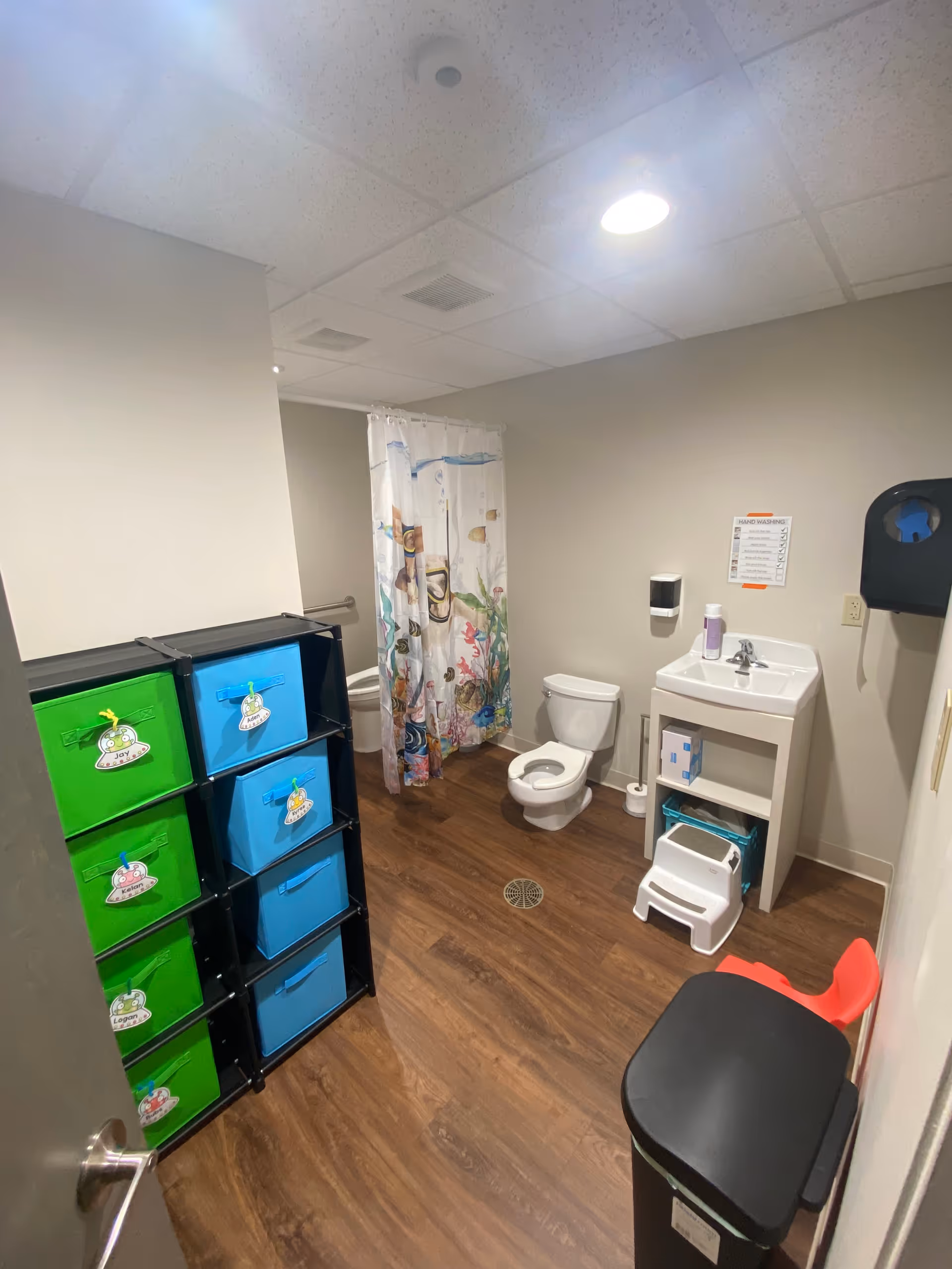 Small bathroom in a senior facility featuring toilet, sink, and a fish-patterned shower curtain.