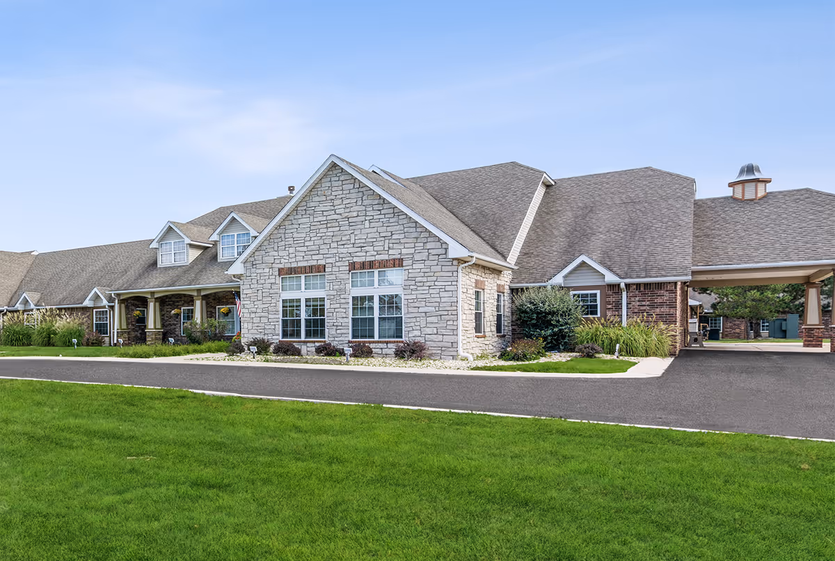 Exterior view of Virginia Place senior living facility with stone facade, driveway, and green lawn.