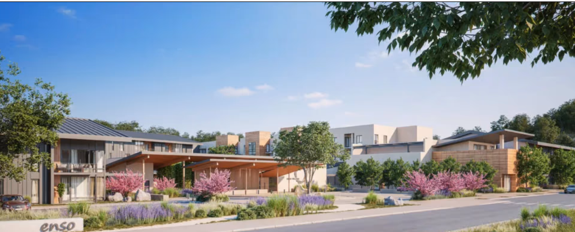 Modern senior living facility front with a covered entrance, landscaped beds and flowering shrubs under a clear blue sky.