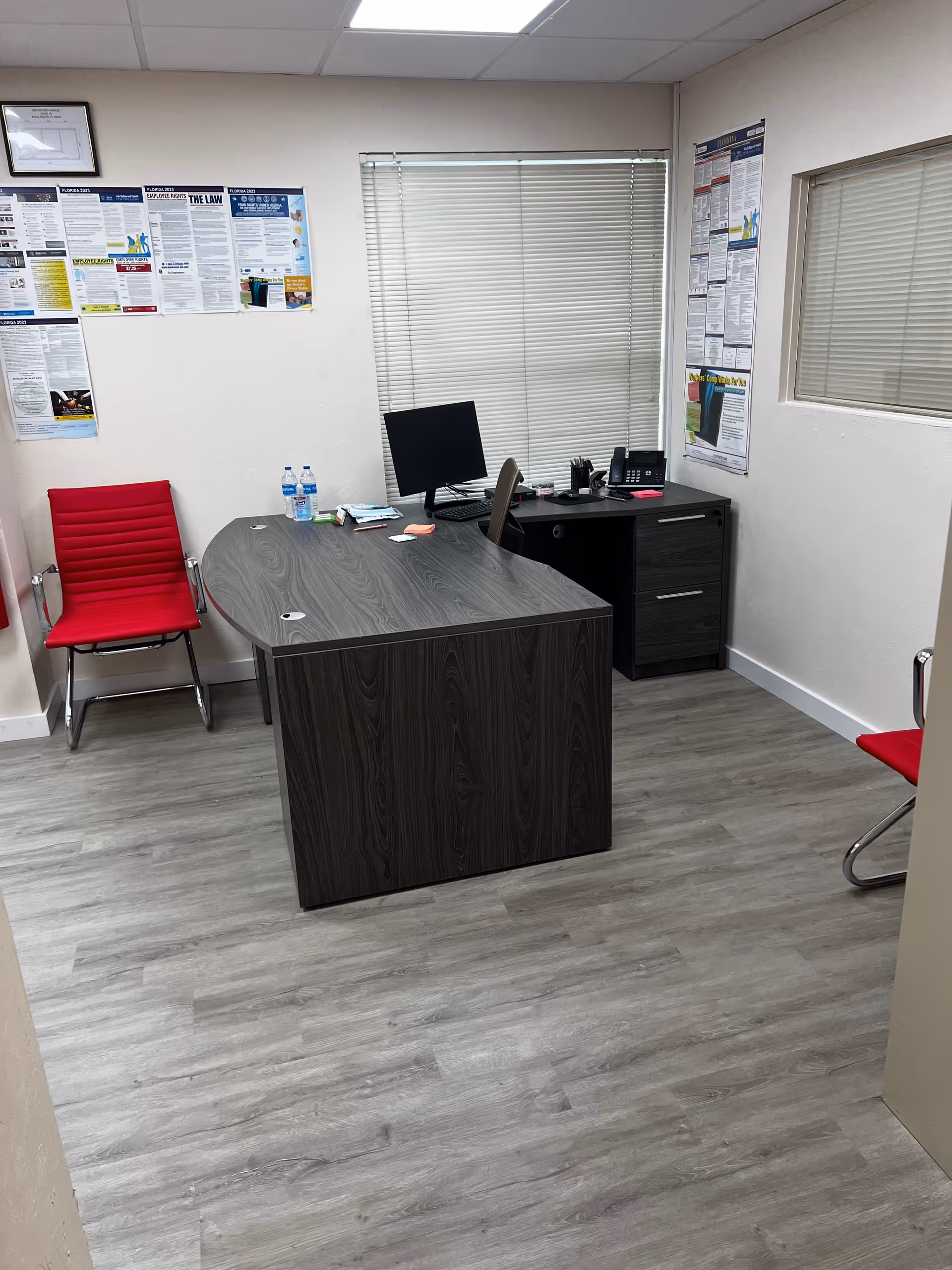 Small office with dark wood desk, red chairs, computer, and wall posters.
