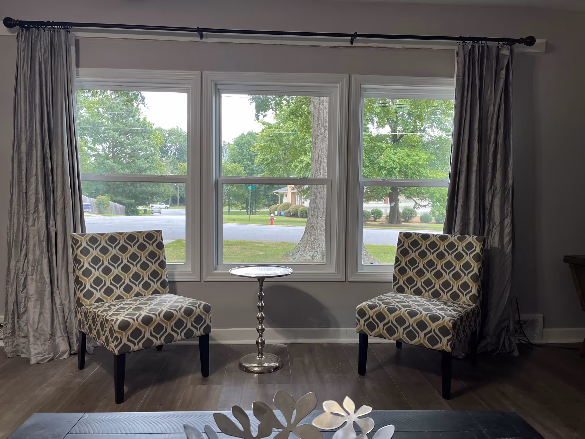 Two patterned chairs flank a small round table by a large window in a living room.