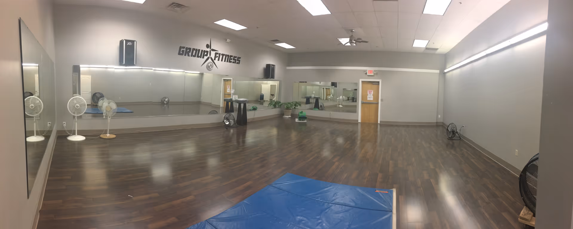Wide view of a rehab gym with mirrors, wooden floors, and exercise mats.
