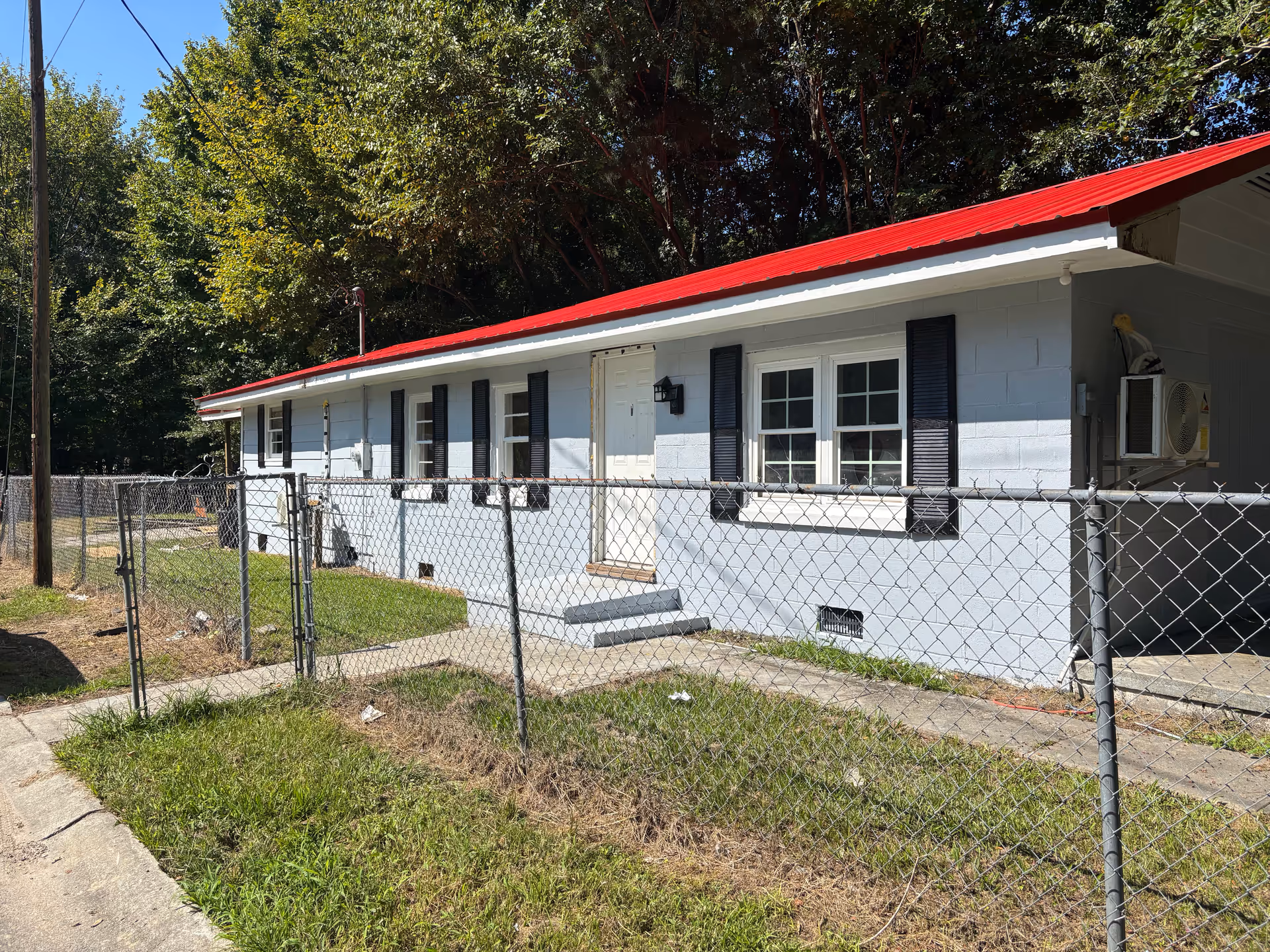 A single-story building with a red metal roof, chain-link fence, and light blue exterior.