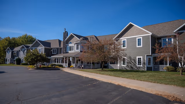 Exterior view of a multi-unit assisted living facility with parking and trees.
