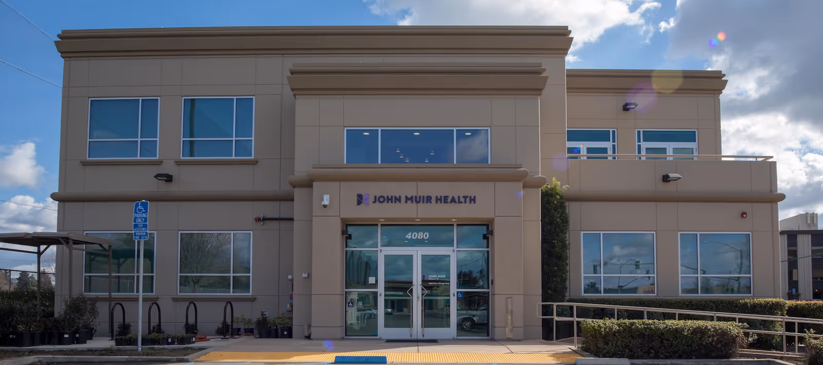 Two-story beige building with glass entrance and John Muir Health signage, accessible ramp.