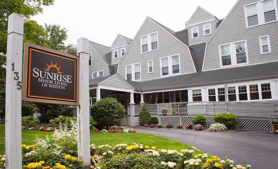 Front exterior of Sunrise Senior Living of Weston with sign and landscaped entrance.