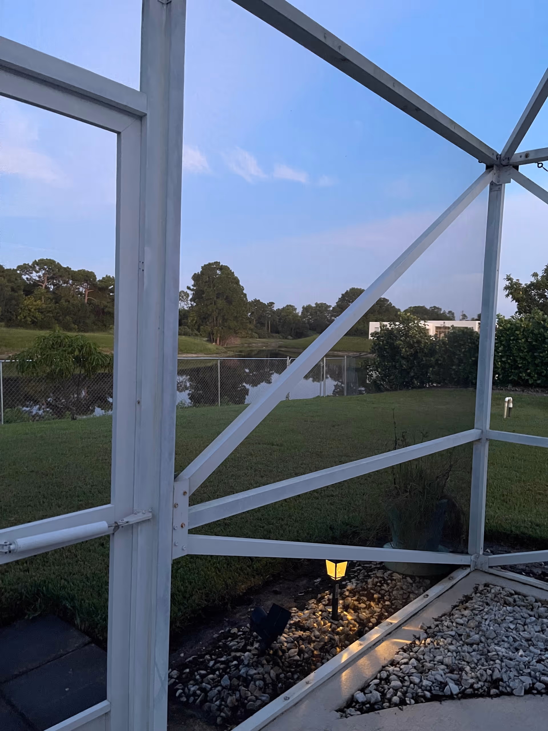 White metal frame of a screened porch overlooking a grassy yard and pond