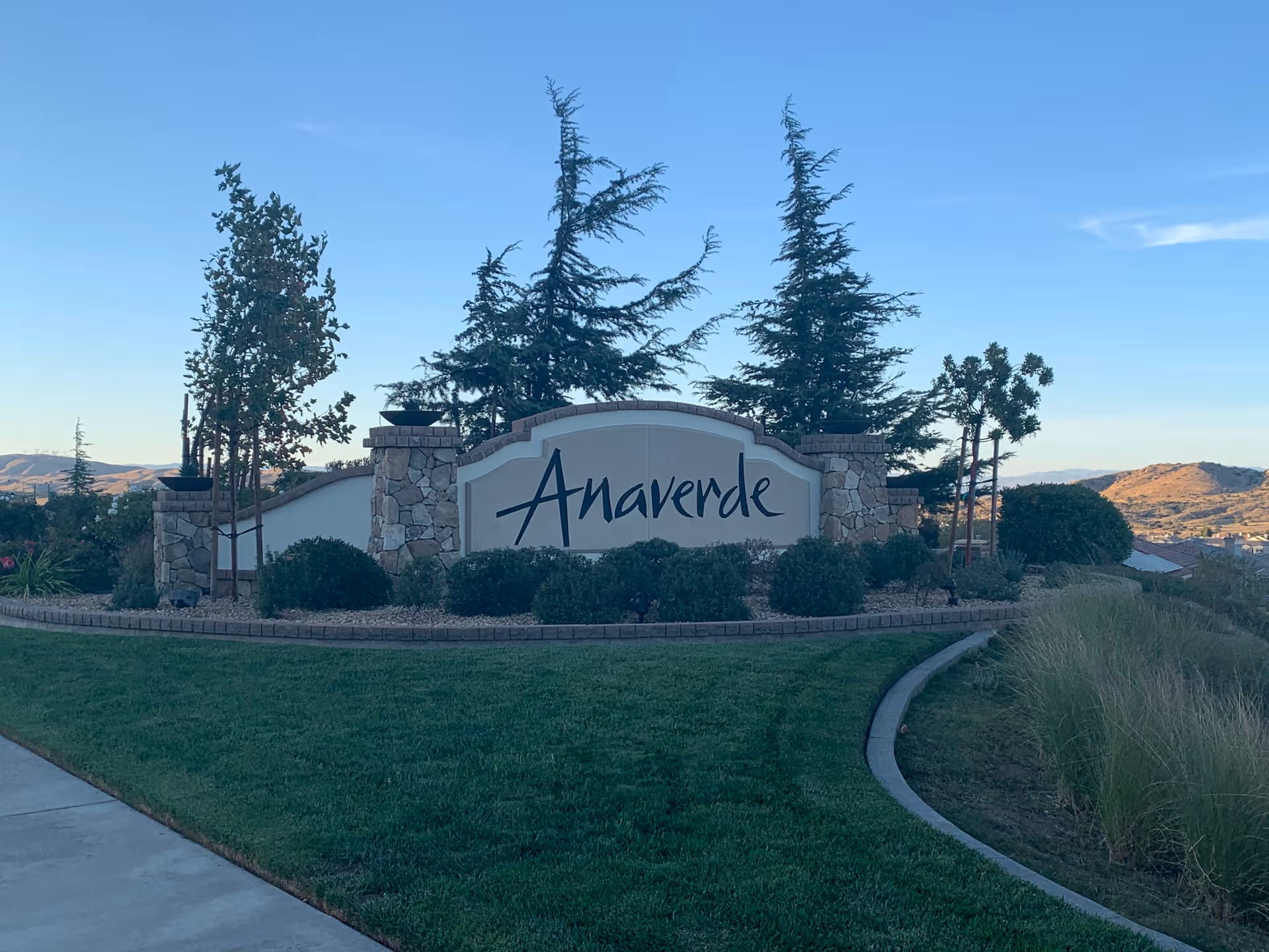 Stone entrance sign reading Anaverde Villa surrounded by shrubs and tall trees.