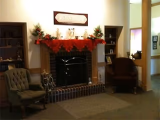 A cozy living room at Belgium Gardens features a lit fireplace flanked by chairs and decor.