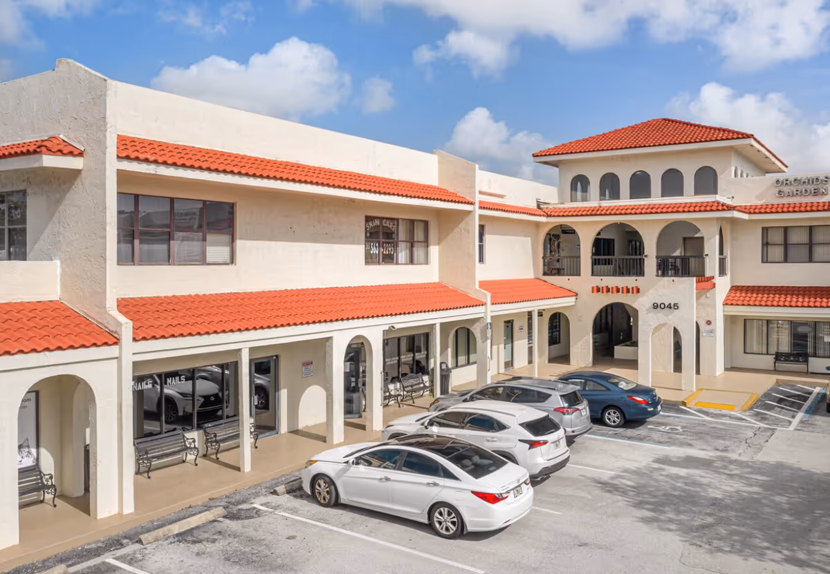 Exterior view of a senior living facility with red-tiled roofs and a parking lot.