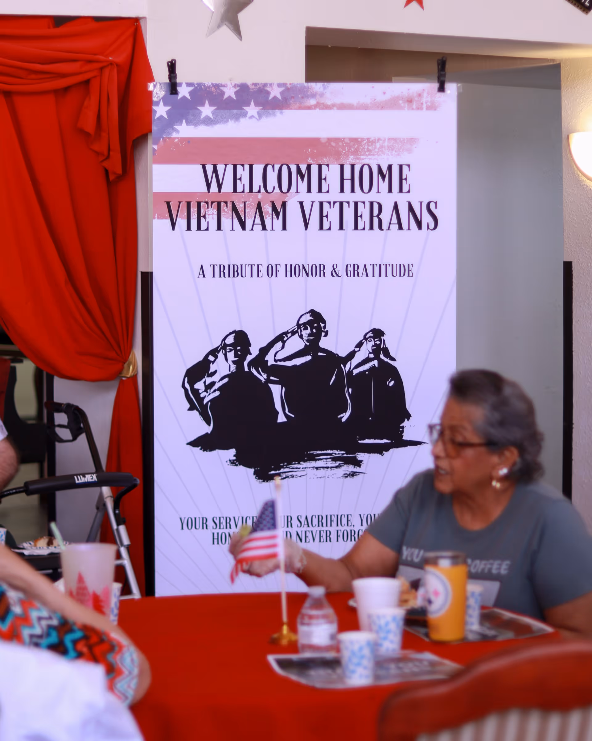 Banner reading Welcome Home Vietnam Veterans at a table with cups and a person.