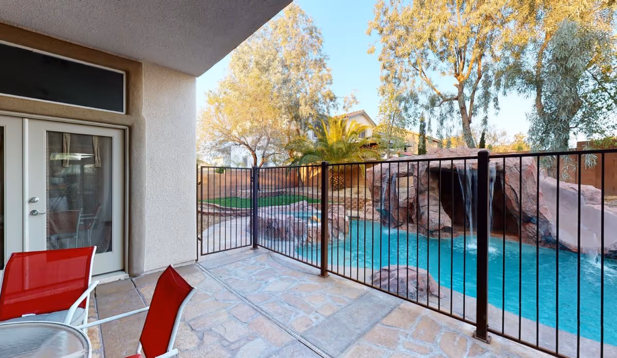 Patio with red chairs overlooking a fenced pool and rock waterfall.