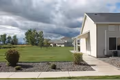 Exterior view of an assisted living facility with lawn, walkway, and cloudy sky.
