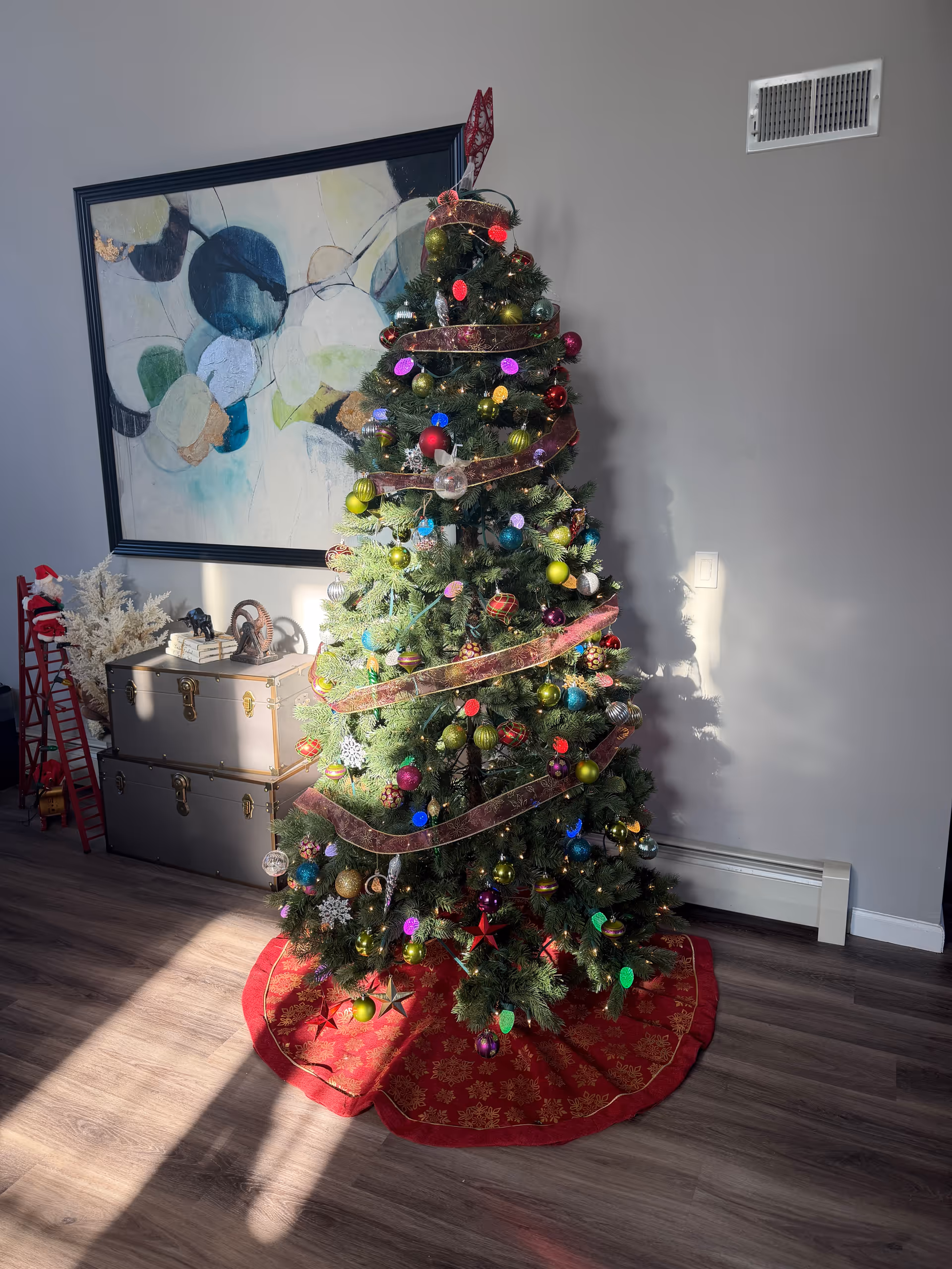 A decorated Christmas tree stands inside a modern living area with sunlight on the floor.