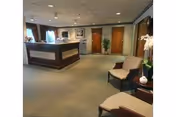 Lobby reception area with a dark wood front desk, chairs, plants, and framed art.