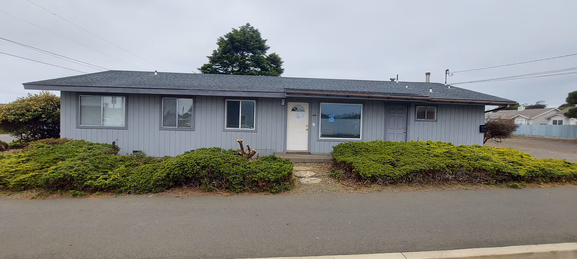 Single-story Oceanside Care Home exterior with windows and trimmed shrubs along the front