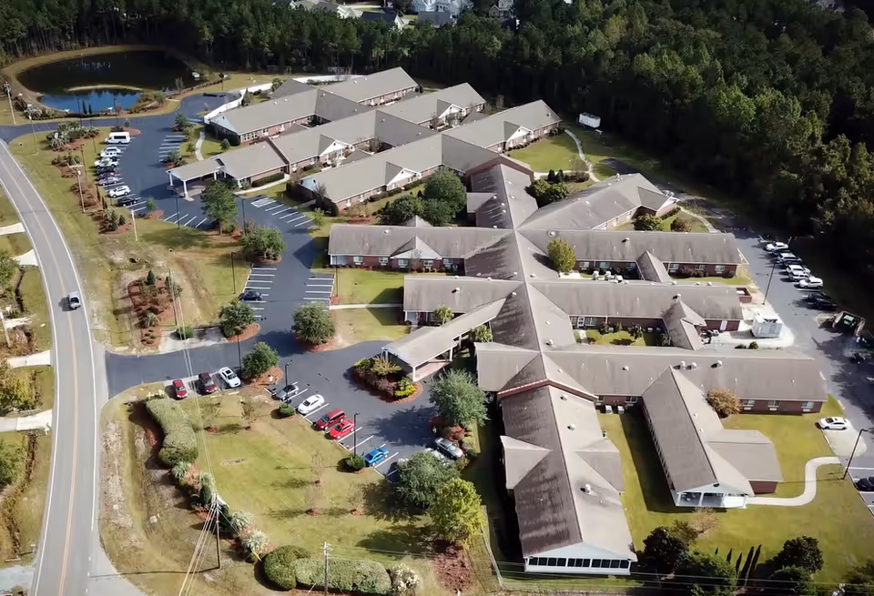 Aerial view of a multi-building senior living campus with parking lots and surrounding trees.