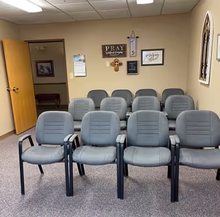 Rows of gray chairs in a small prayer room with religious decor.