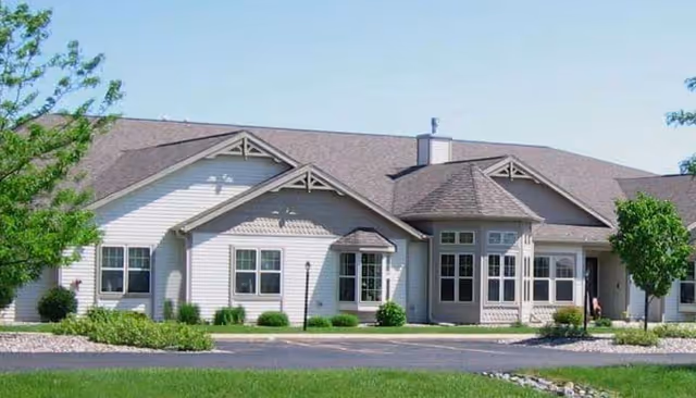 Exterior view of Copperleaf Assisted Living of Schofield facility with a light-gray building, landscaping, and driveway.
