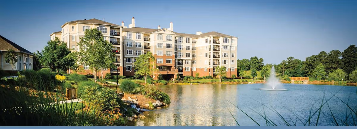 The Cypress Of Raleigh senior living building sits beside a landscaped lake with a fountain.