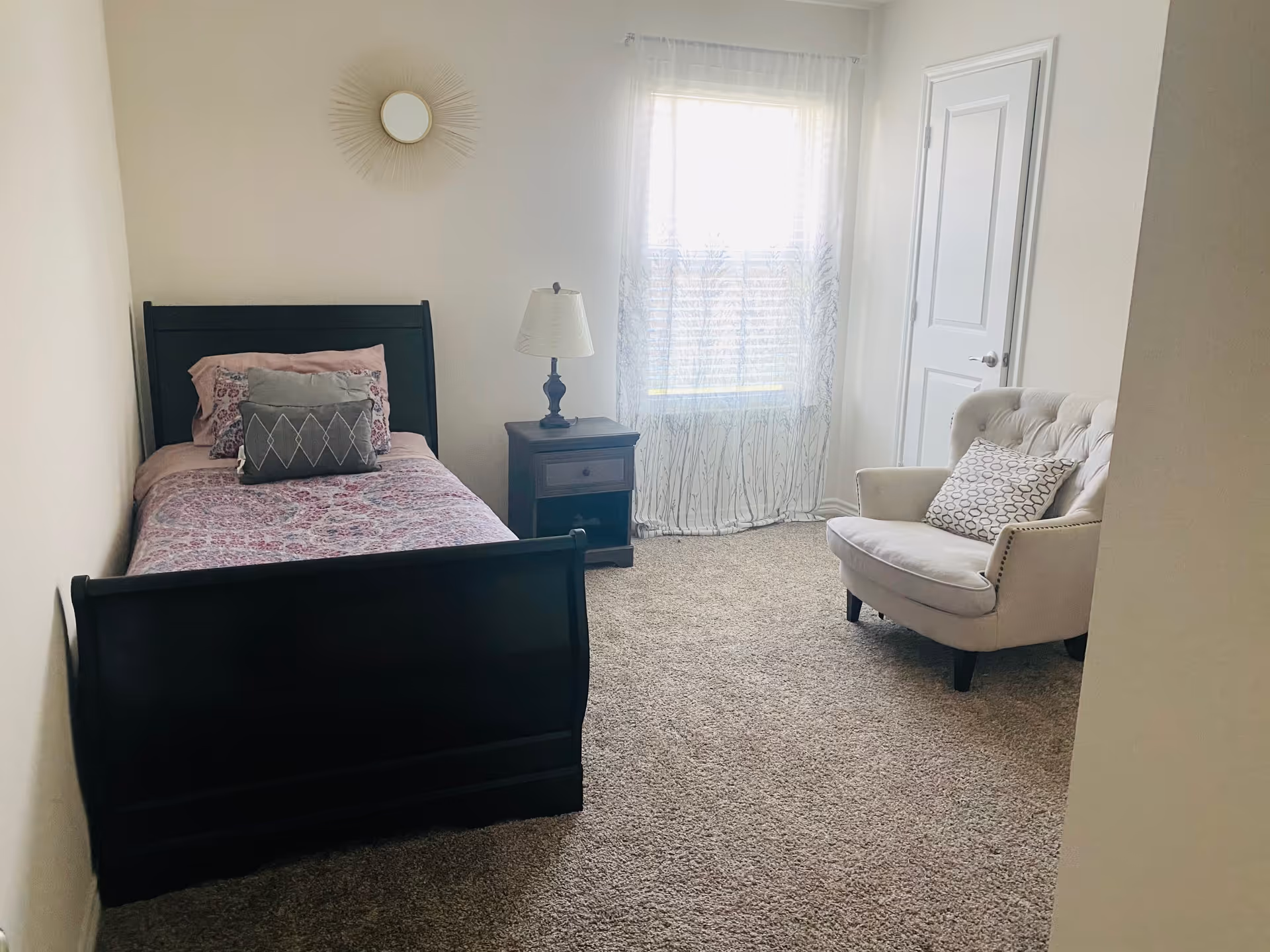 A dark wooden bed with nightstand, window, and a plush chair in a bright bedroom.
