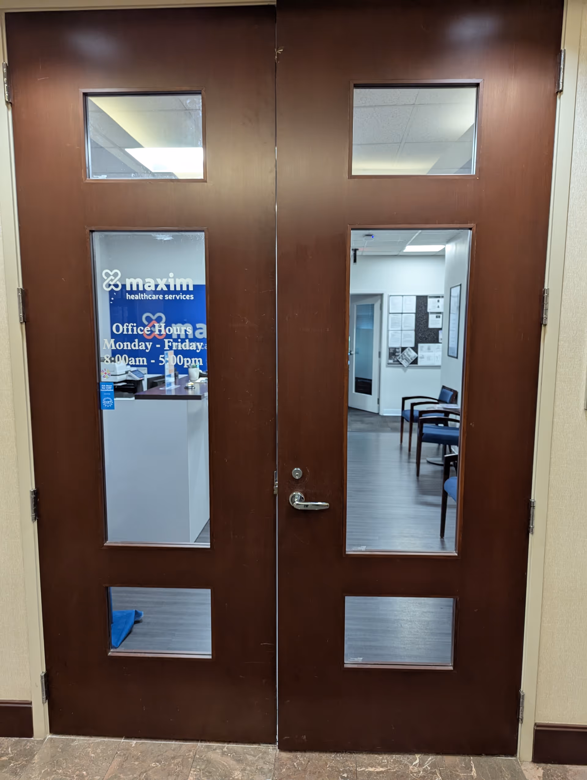 Two brown doors with glass panels reveal an office area with desks and chairs.