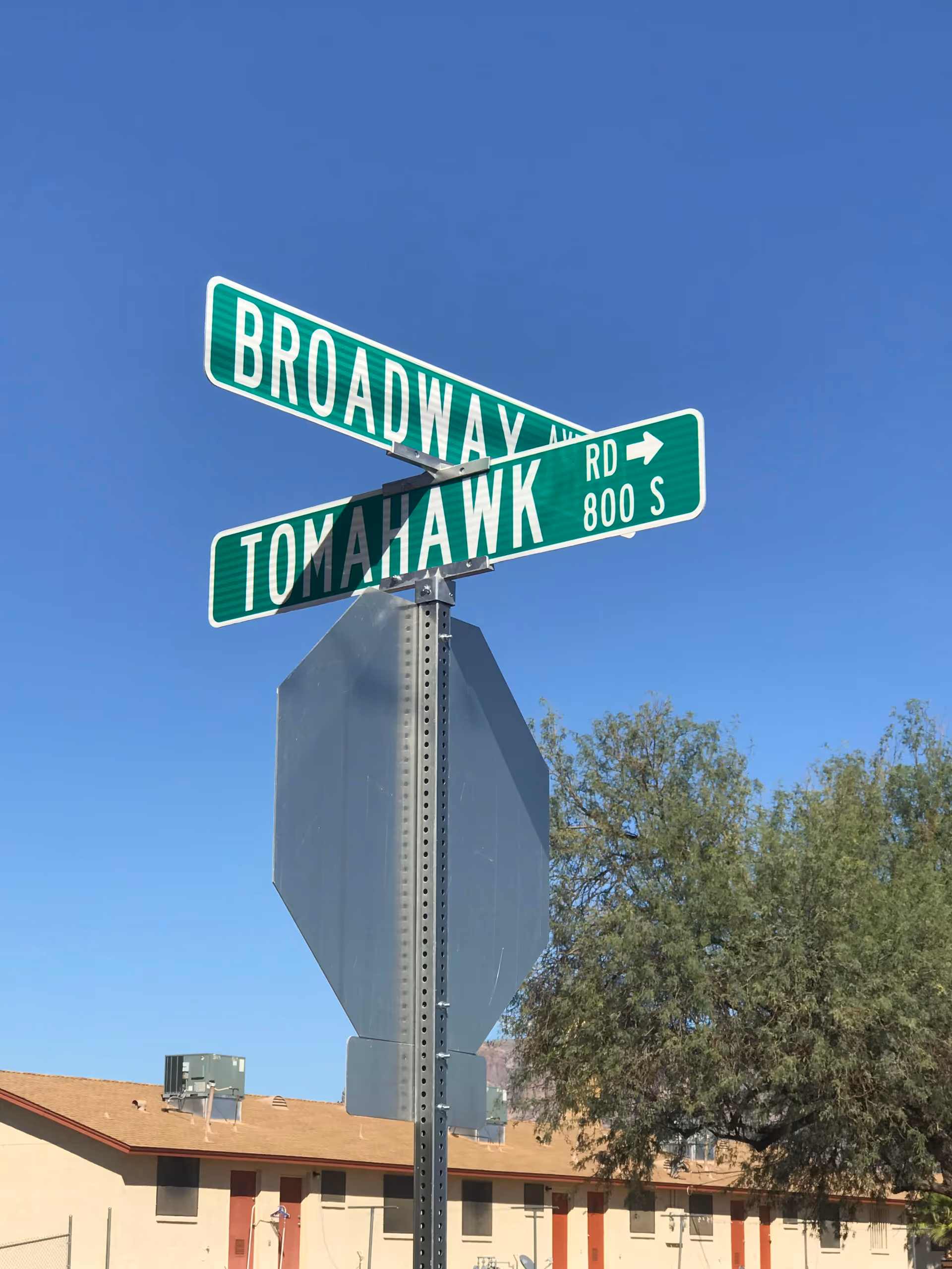 Two green street signs reading Broadway and Tomahawk Rd cross under a blue sky.
