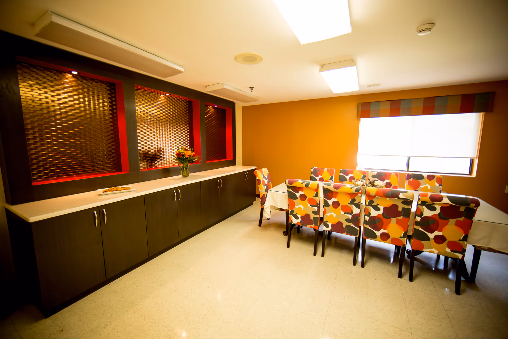 A bright dining area with patterned chairs, a long counter, and a window.