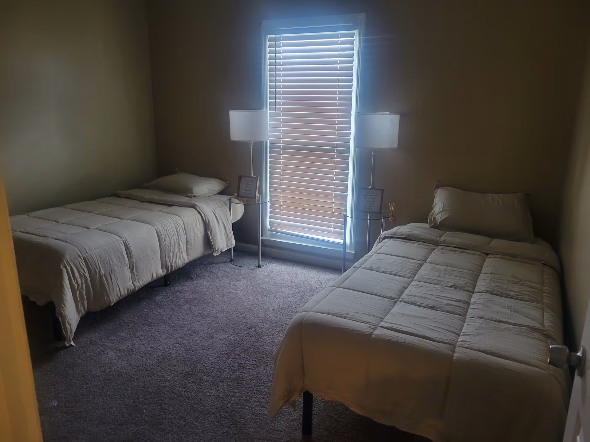 Two twin beds with white bedding sit beside a window with blinds.
