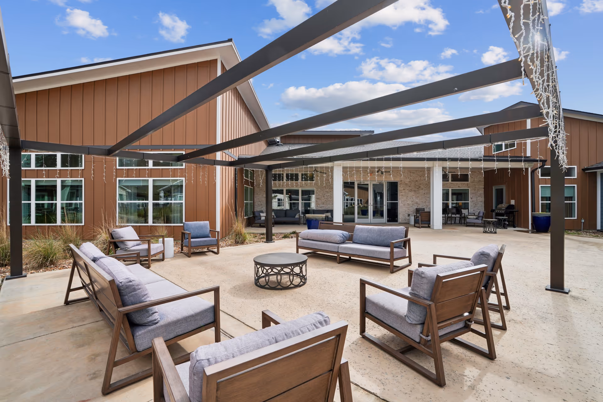 Outdoor patio seating area with couches around a central round table beneath string lights.