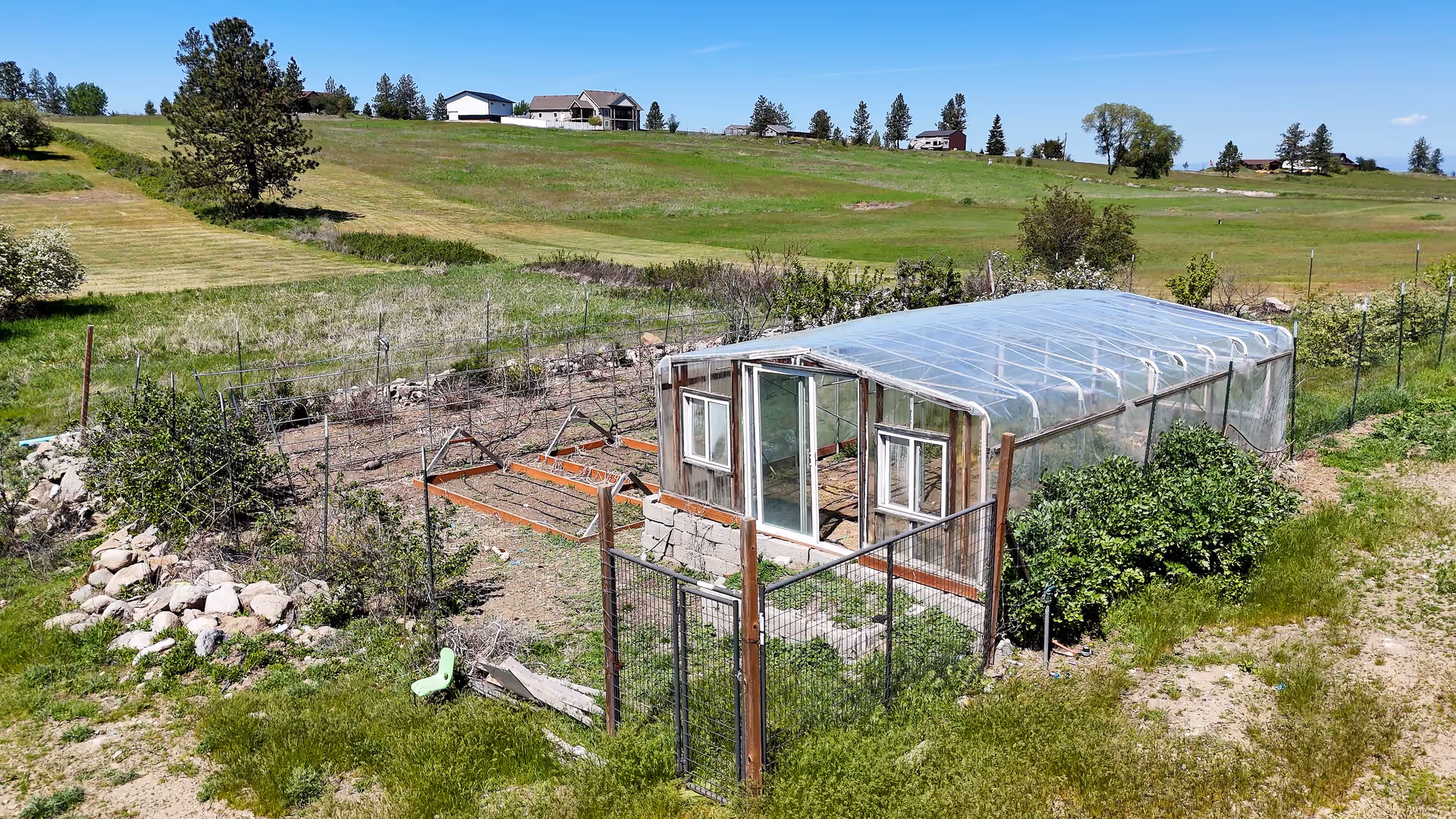 Rural yard with a plastic-covered greenhouse surrounded by a wire fence