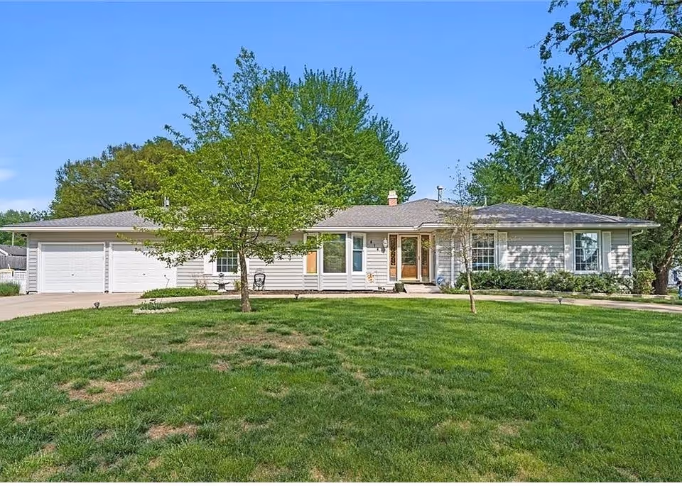 A single-story facility with a green lawn, trees, and a driveway in front.