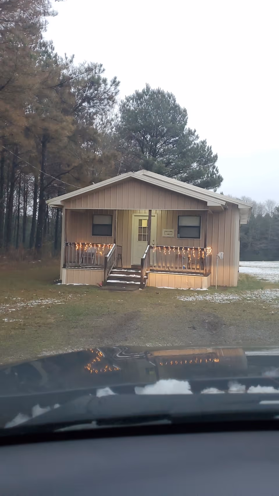 Small beige cottage-style building with string lights on a front porch, trees in background.