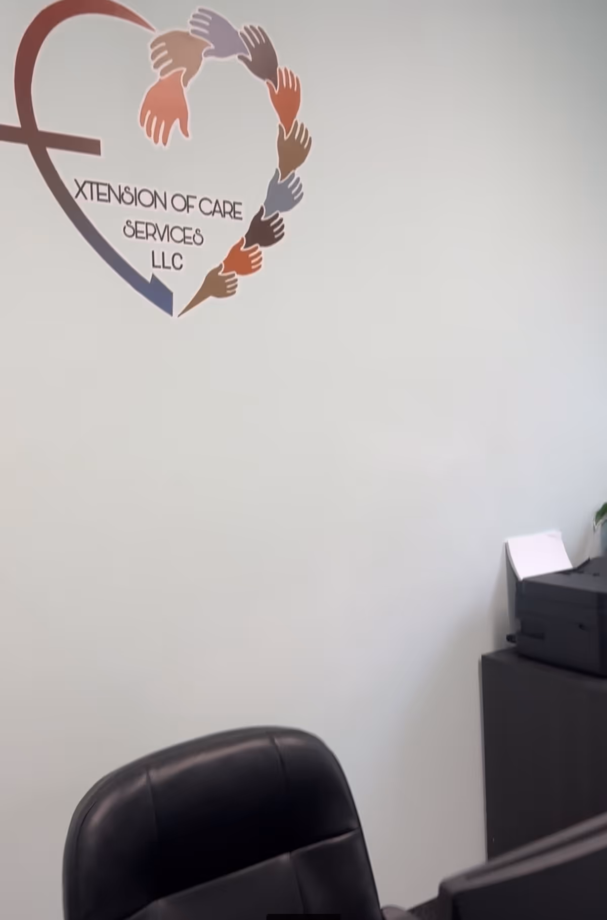 Office corner with Xtension of Care Services LLC logo on wall and a black chair.