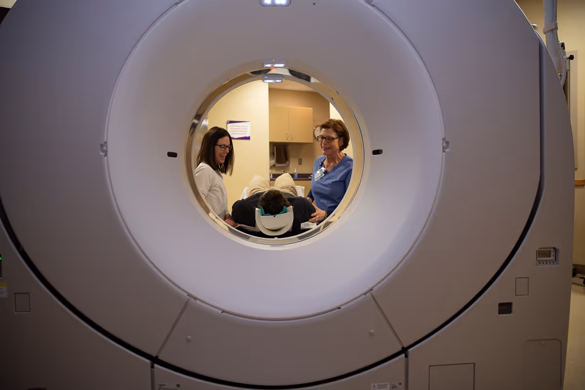 In a medical imaging room, staff assist a patient inside a large CT scanner.