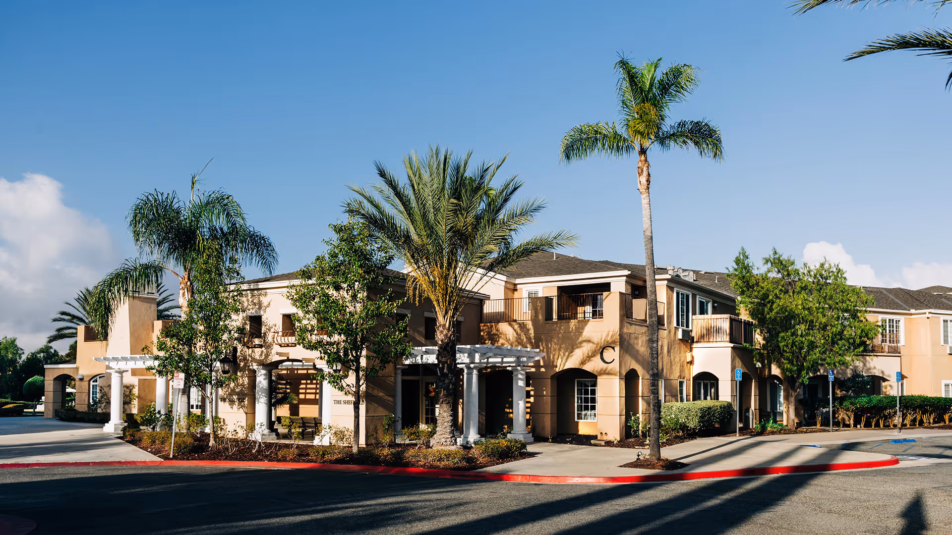 Exterior view of a senior living building with palm trees and a curved entrance.