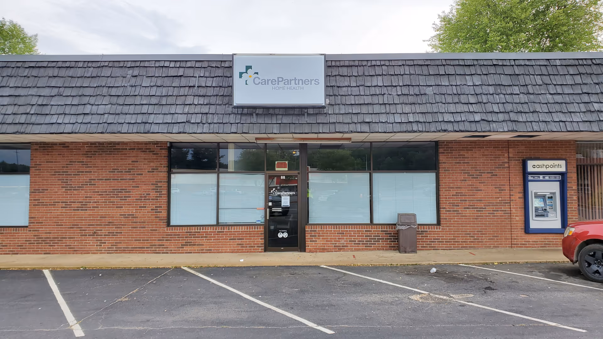 Brick storefront with CarePartners Home Health sign and a parking lot in front.