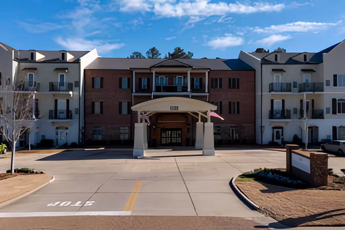 Exterior front entrance of a multi-story senior living building with a covered porte-cochère and driveway.