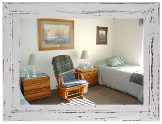Bedroom in a senior care home featuring a bed, chair, and two lamps.