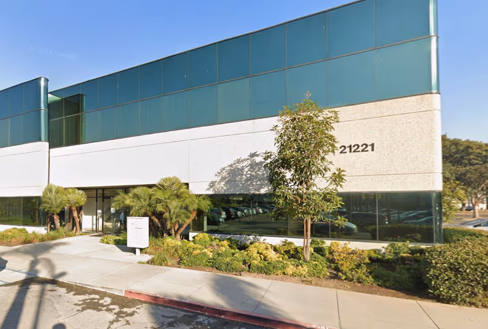 Modern glass-front building with landscaping and a driveway in front, address 21221.