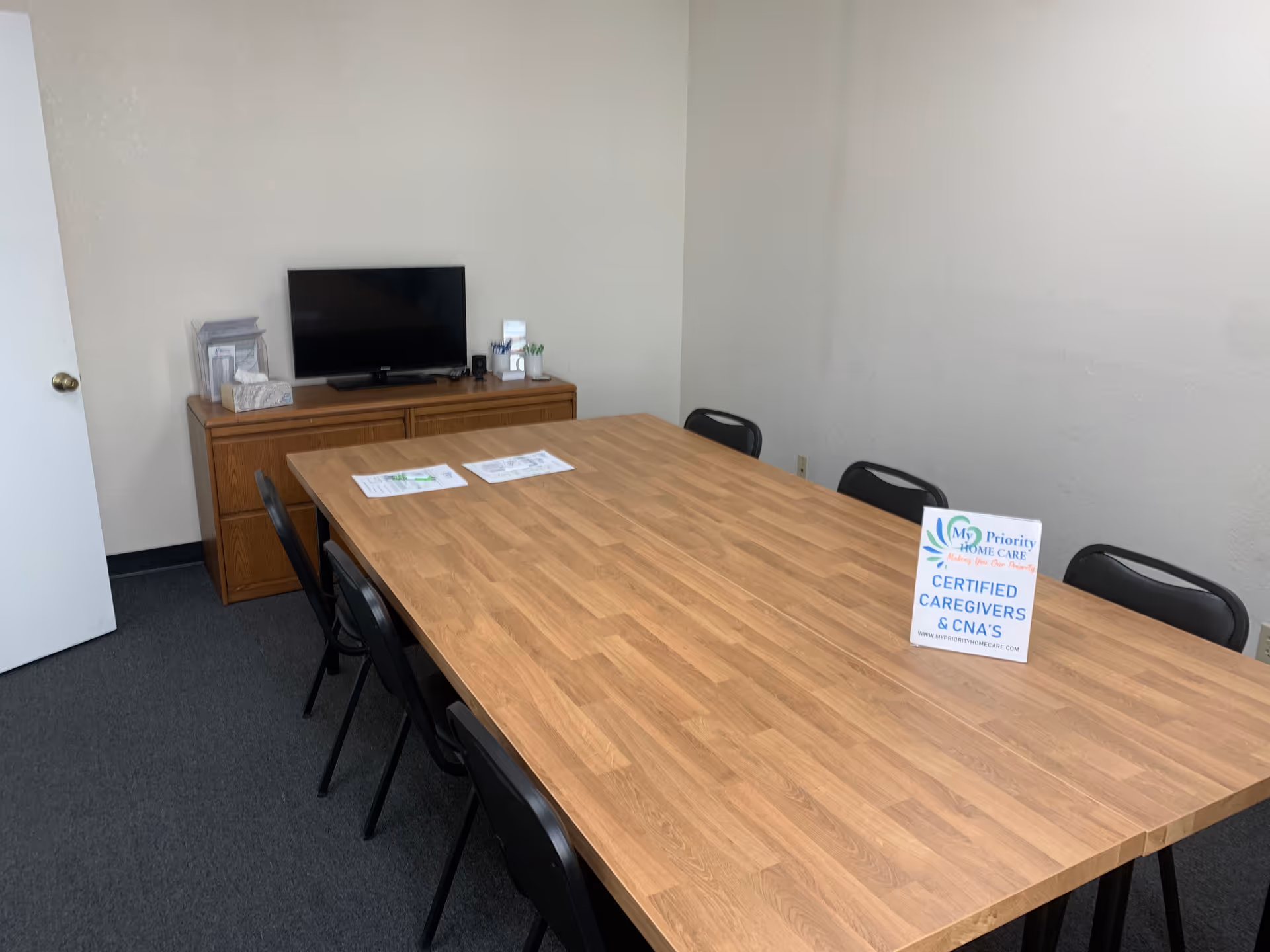 A conference room with a wooden table, chairs, and a TV on a cabinet.