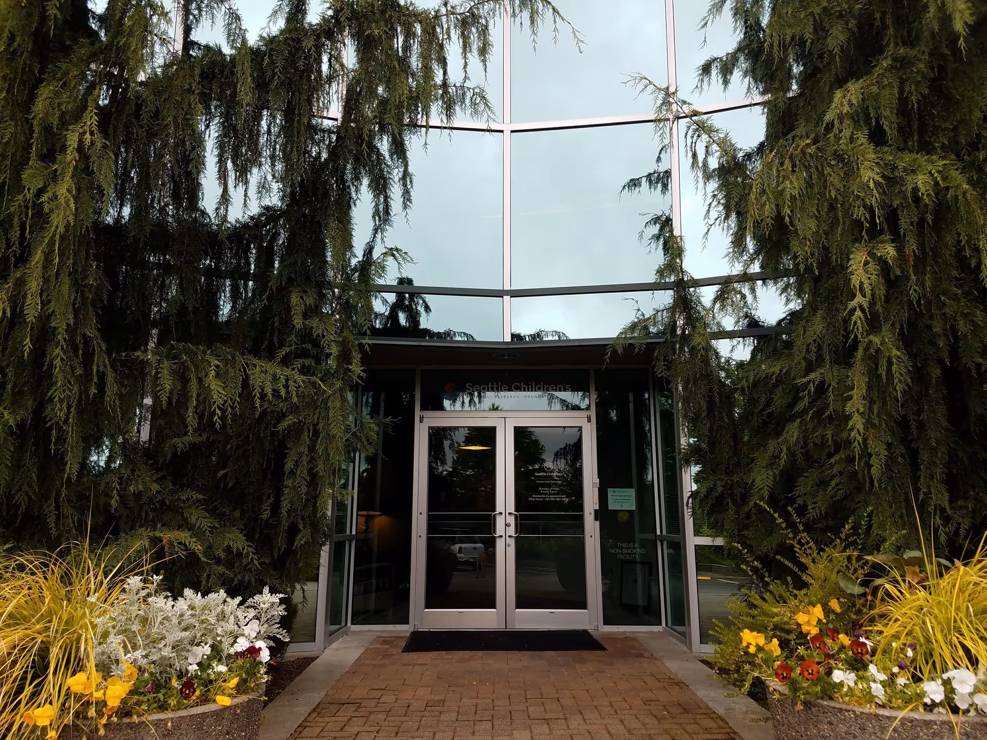 Glass-front entrance of Seattle Children's Home Care Services framed by tall evergreens