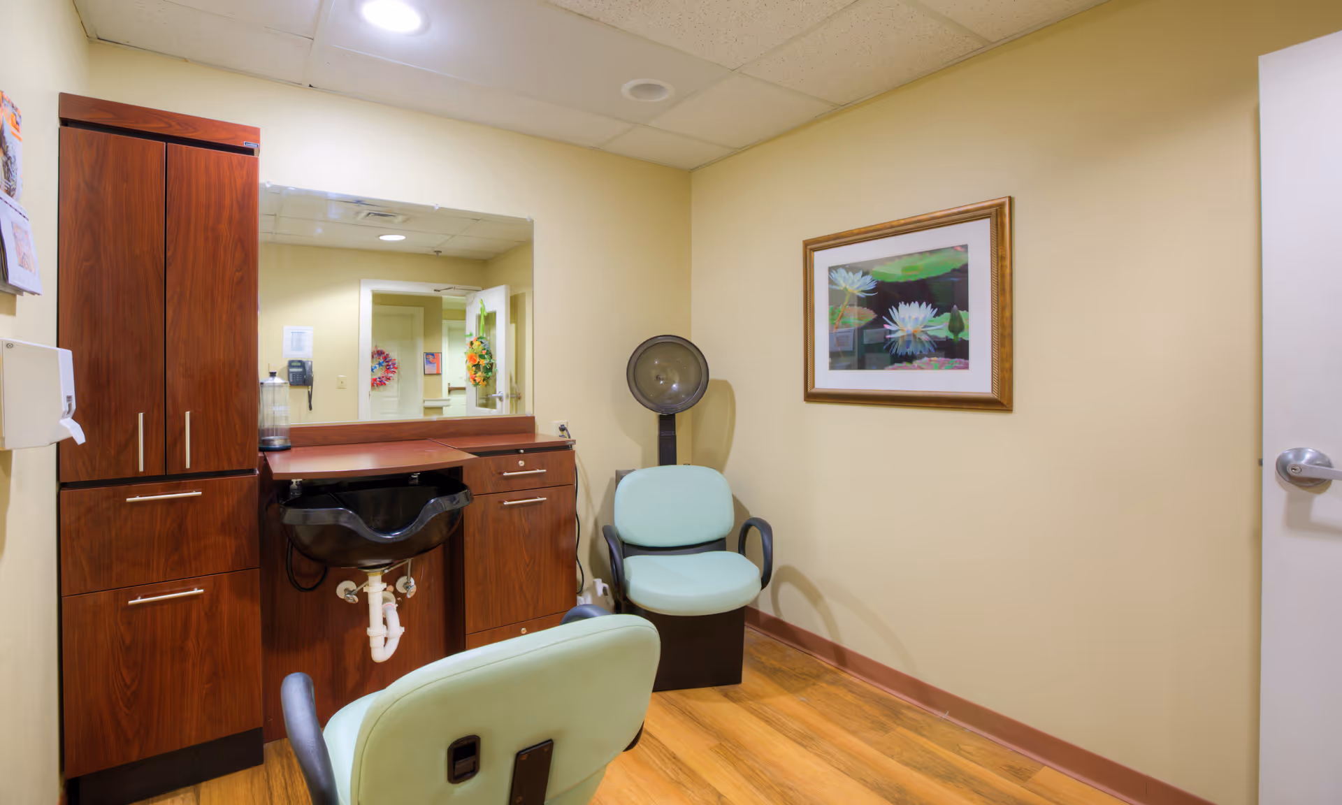 Salon area with wooden cabinets, mirror, and mint chairs in a clinical interior.