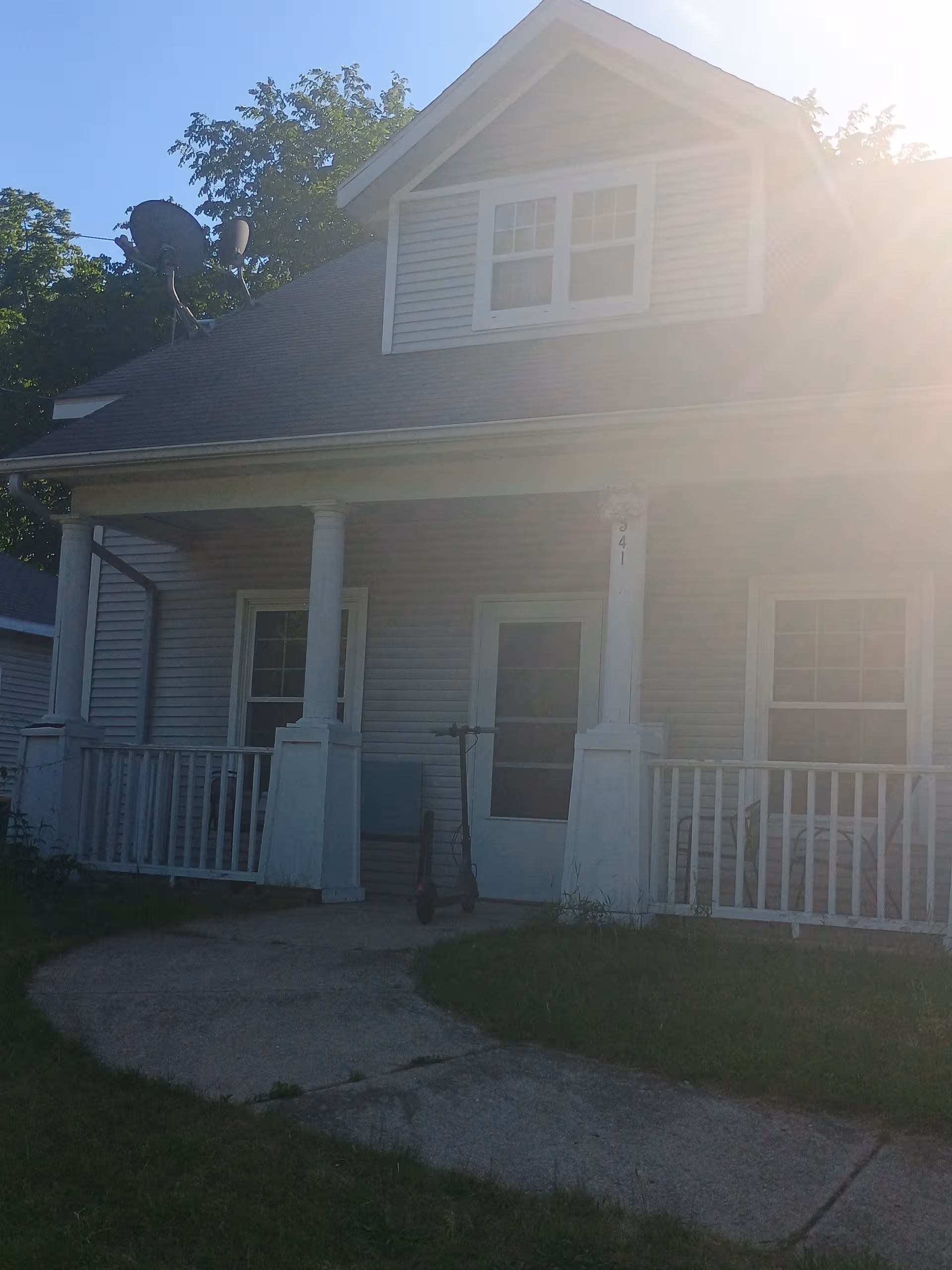 Front view of a light-blue two-story house with a porch and scooter.