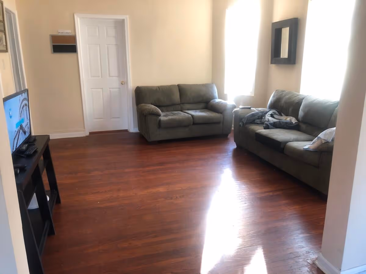 Living room with two green couches, a TV stand, and sunlit windows.