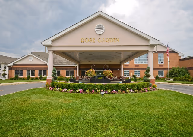 Front entrance of Rose Garden Nursing and Rehabilitation Center with landscaped lawn and seating.