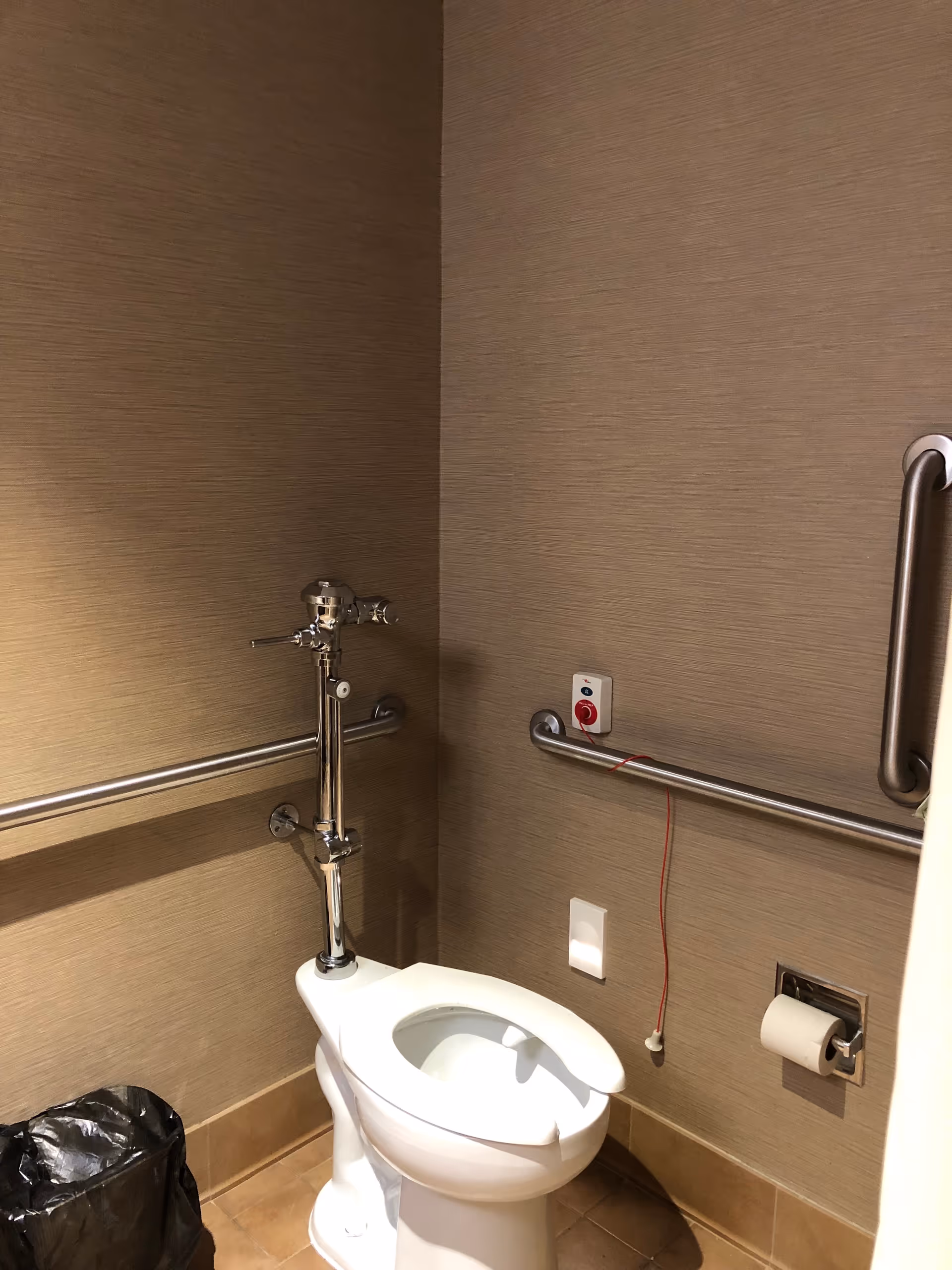 Accessible bathroom with grab bars, a toilet, emergency pull cord, and paper holder.