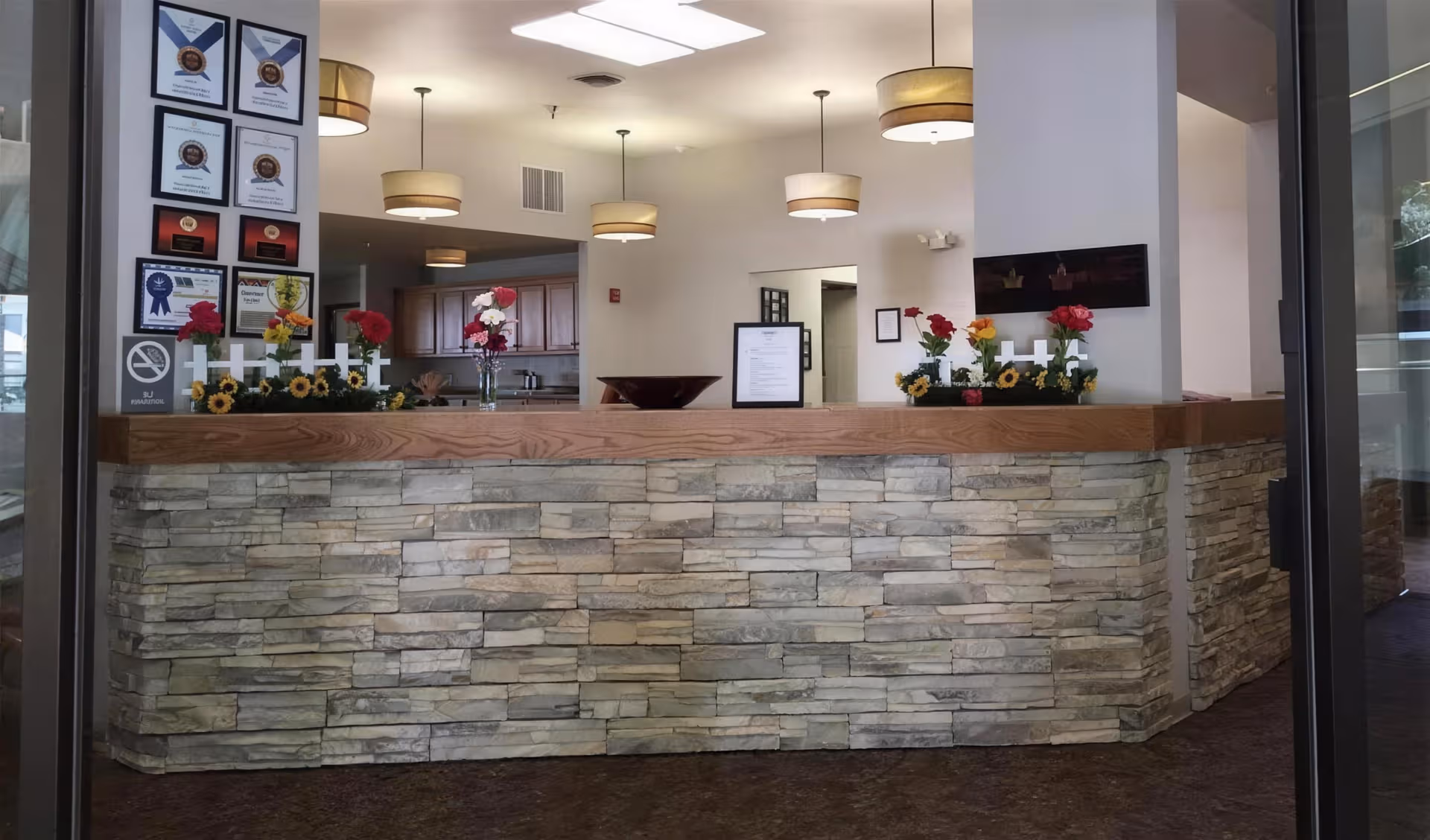Interior reception desk with stone base, flowers, and certificates in Madison House-Assisted Living lobby.