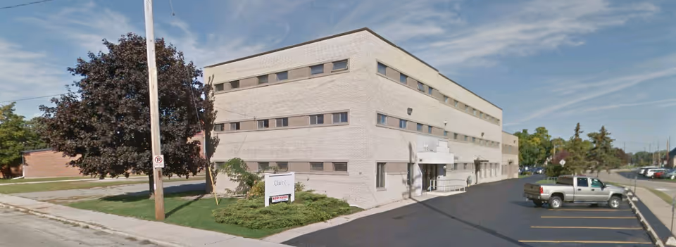 Three-story light brick senior living facility with a front entrance and parking lot.